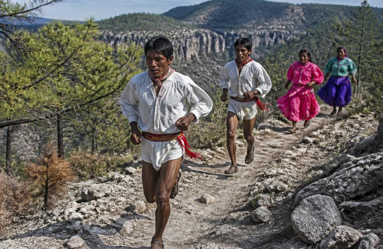 Grupo de corredores rarámuris por un camino de tierra en la sierra.